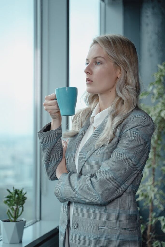 pexels-photo-5717625 A focused businesswoman in a suit holding coffee, gazing outside the office window.