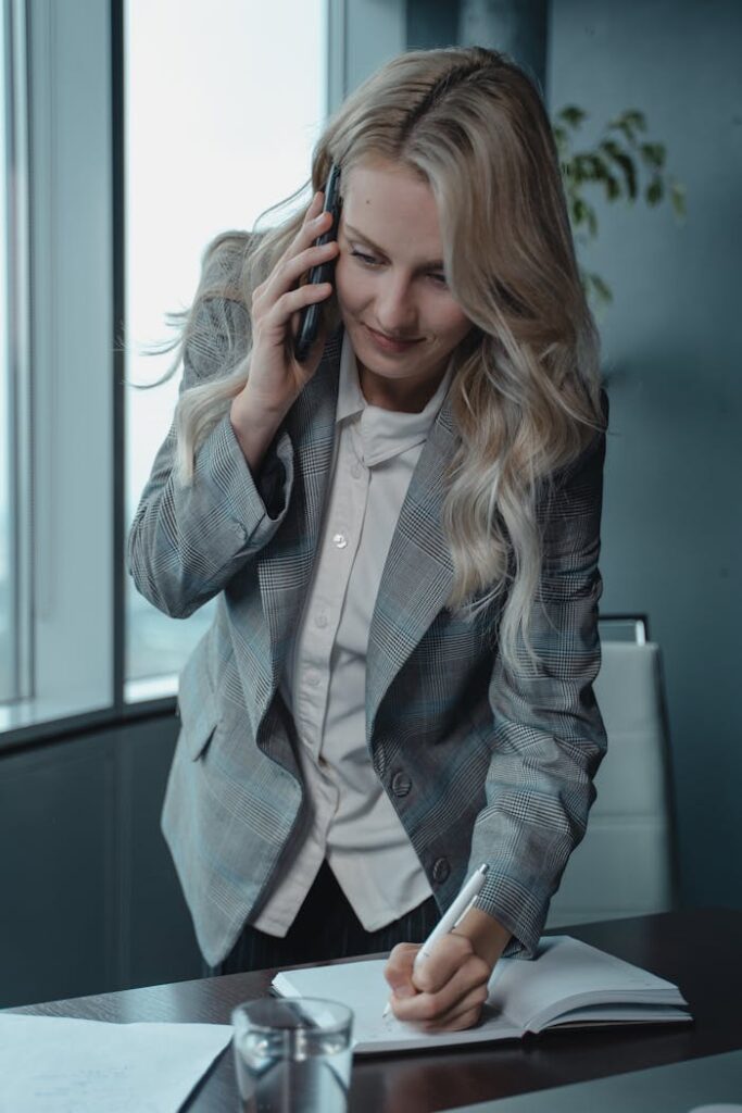 Professional businesswoman multitasking with phone and notes in modern office setting.